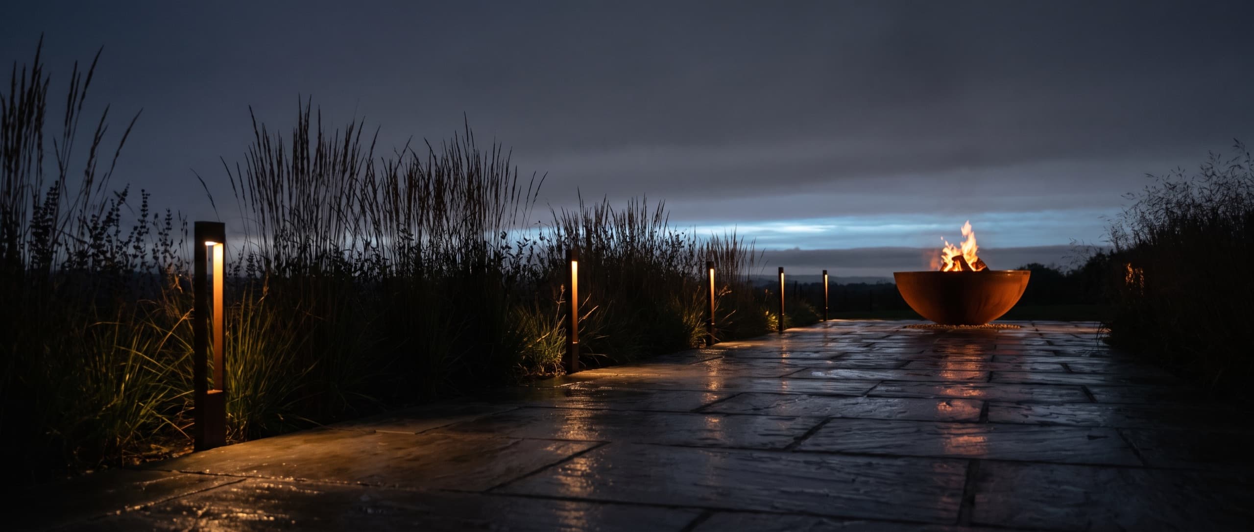 Allée de jardin au crépuscule, bornes lumineuses et brasero au fond